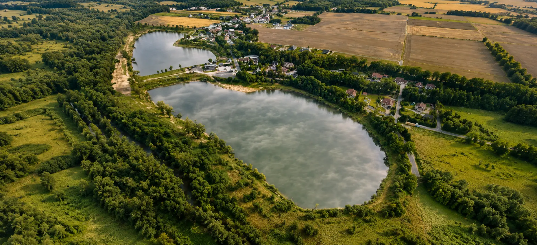 Widok z lotu ptaka na dwa stawy łowiska otoczone polami i lasem